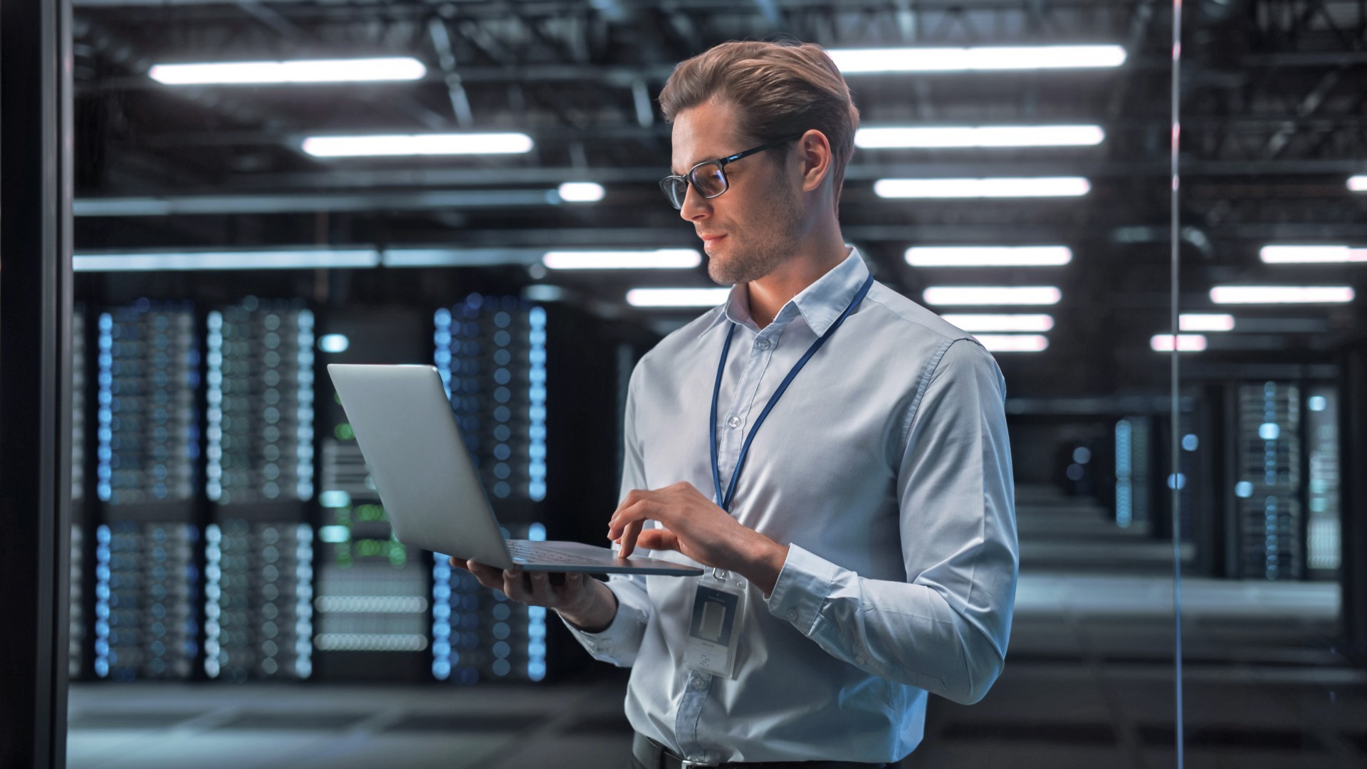 In een datacenter kijkt een man op zijn laptop. Op de achtergrond staan grote serverracks.