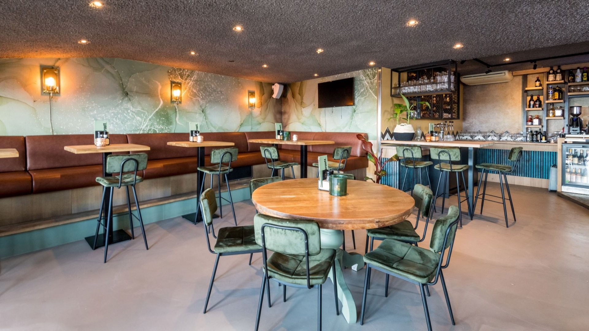 Kijkje in Brasserie Bruutt: aan de zijwand staat een lange bank met daarlangs tafeltje met nog één op de voorgrond. Op de achterwand de toog.
