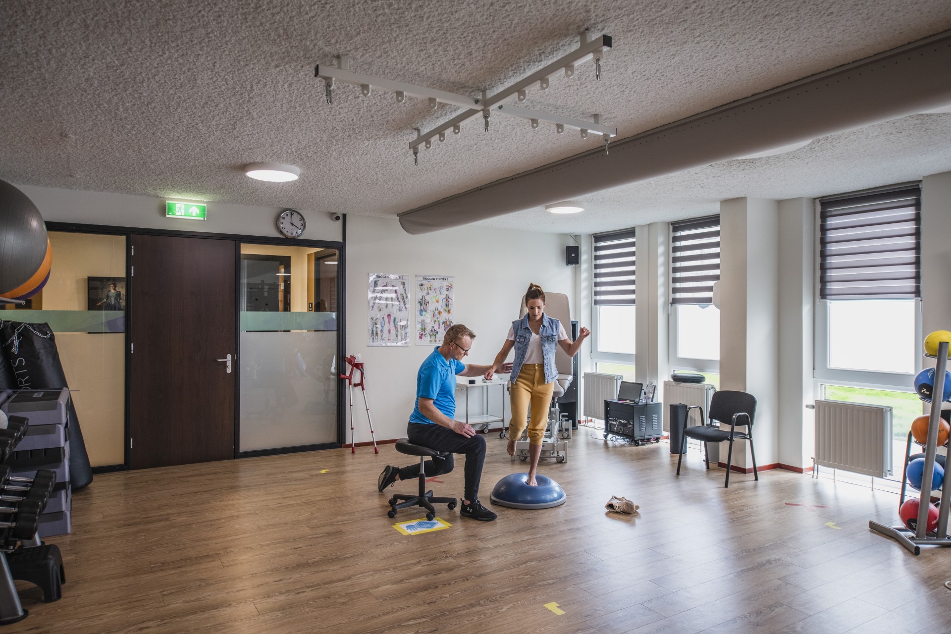 Patiënt doet in een fysiopraktijk oefeningen, waarbij de fysiotherapeut haar begeleidt