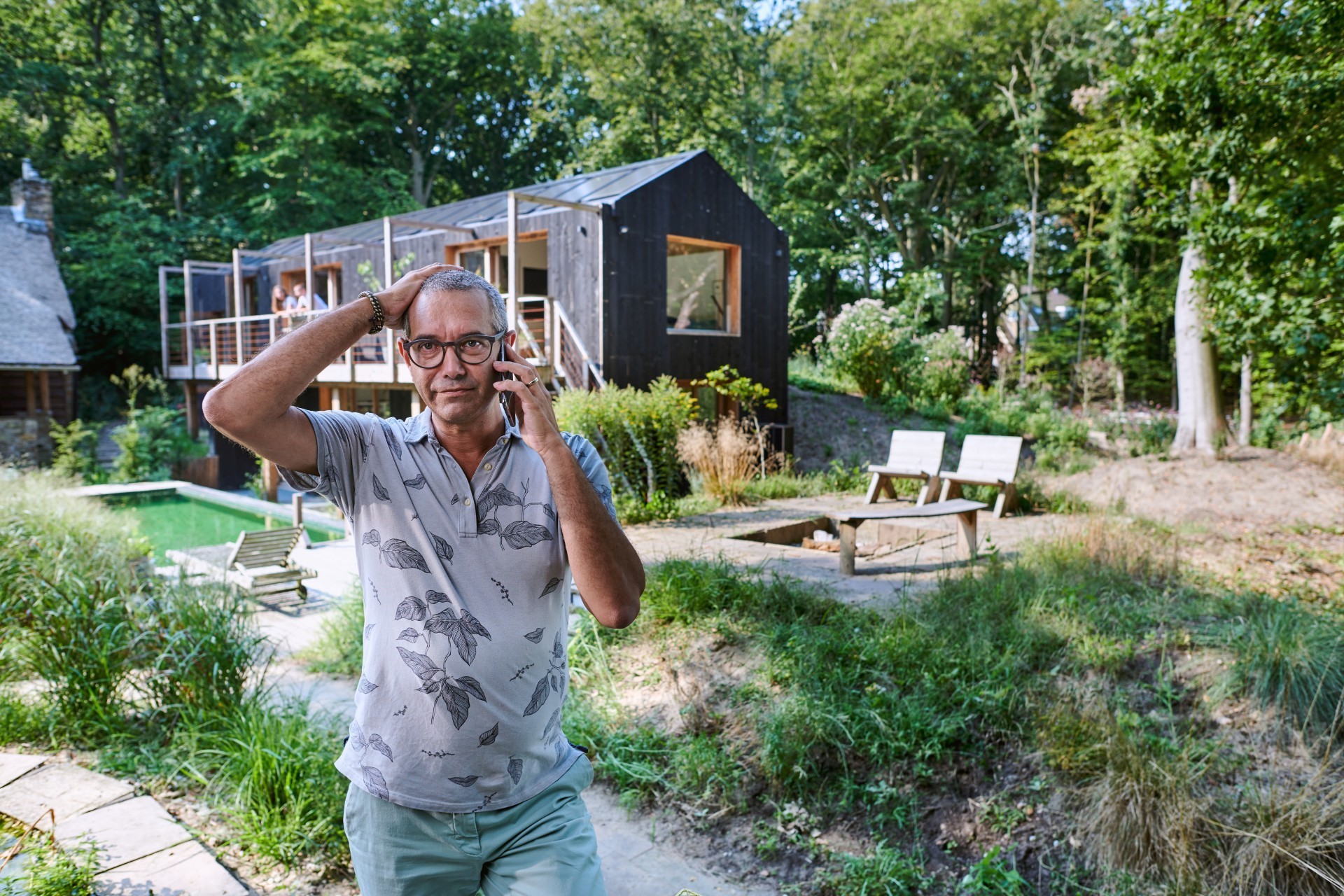 Man staat voor een houten gebouw en heeft telefoon tegen zijn oor gedrukt