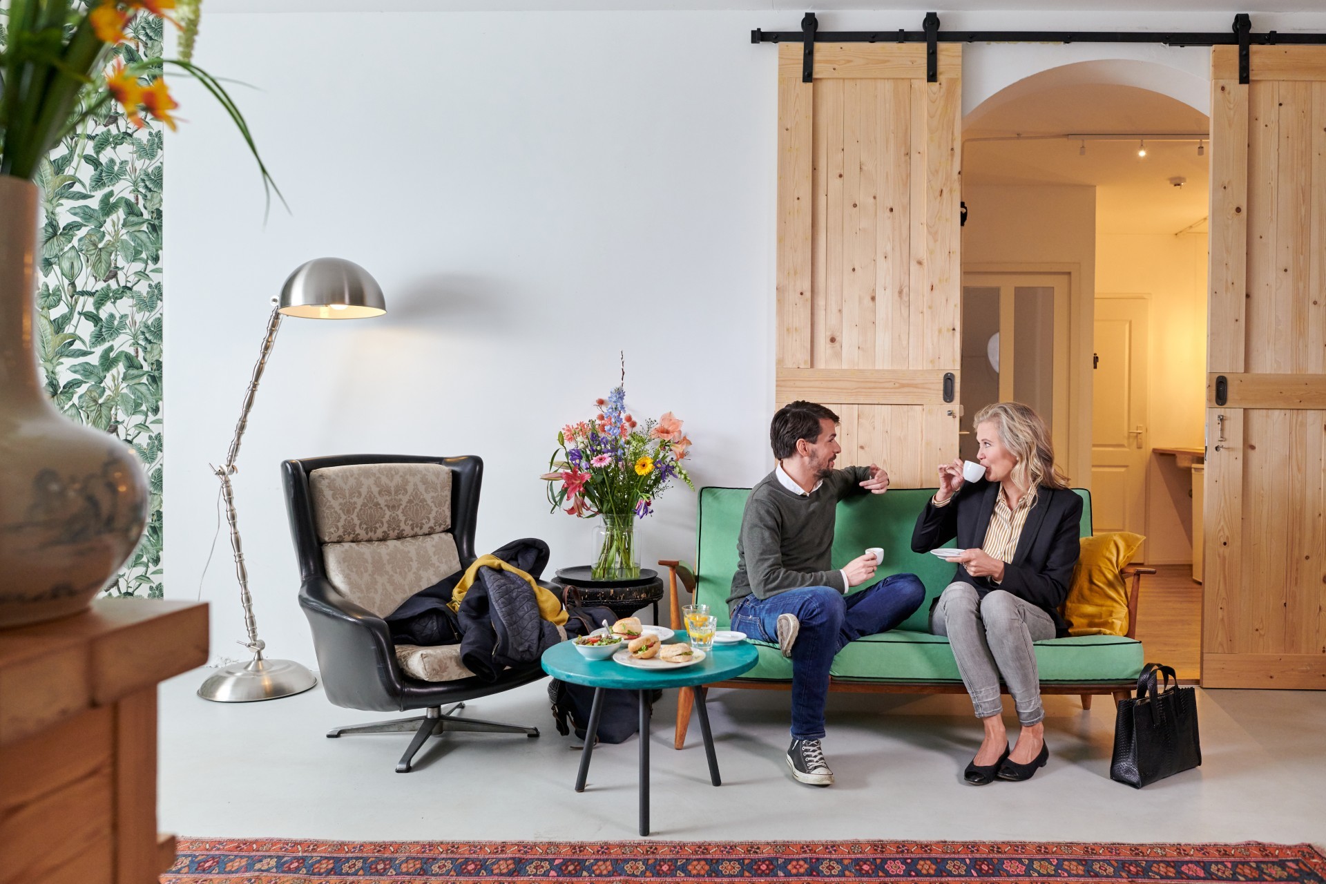 Een zakelijk geklede man en een vrouw zitten op een bank. Ze praten en drinken koffie.