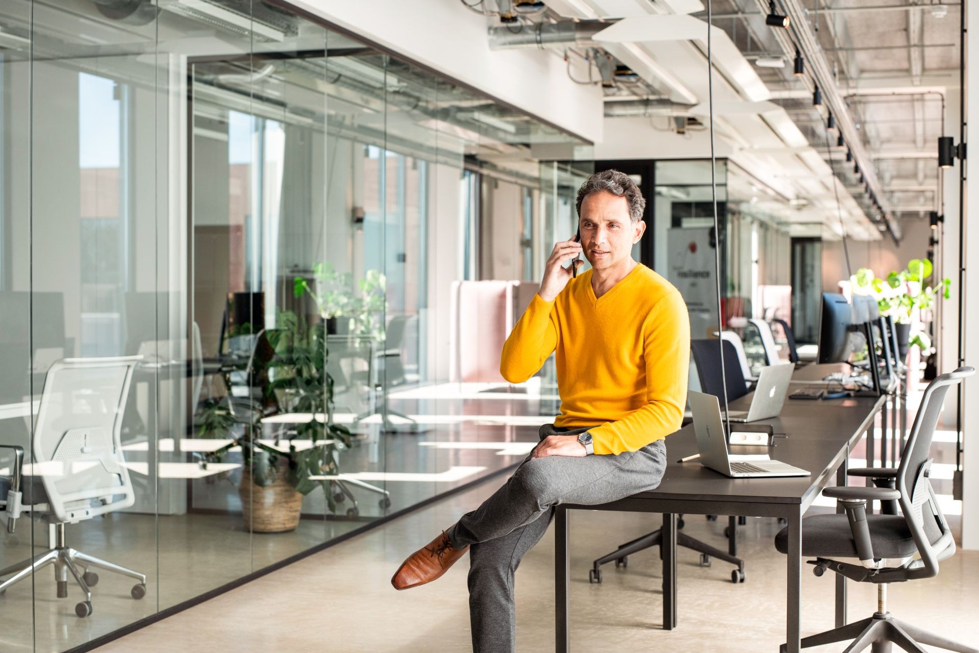 Man zit op kantoor op zijn bureau met telefoon tegen zijn oor, waar hij tegen praat