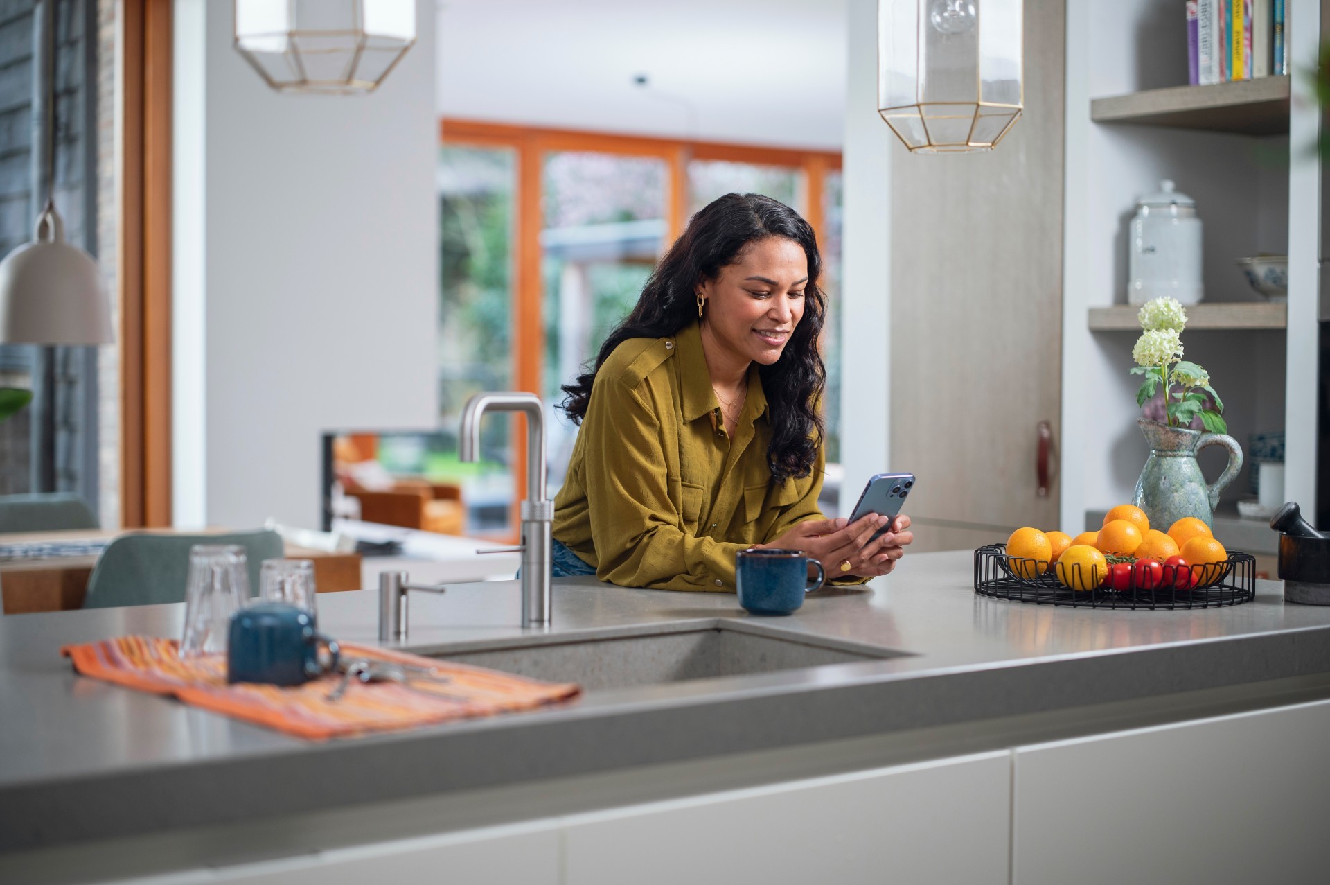 Vrouw aan keukentafel kijkt naar informatie op haar mobiele telefoon