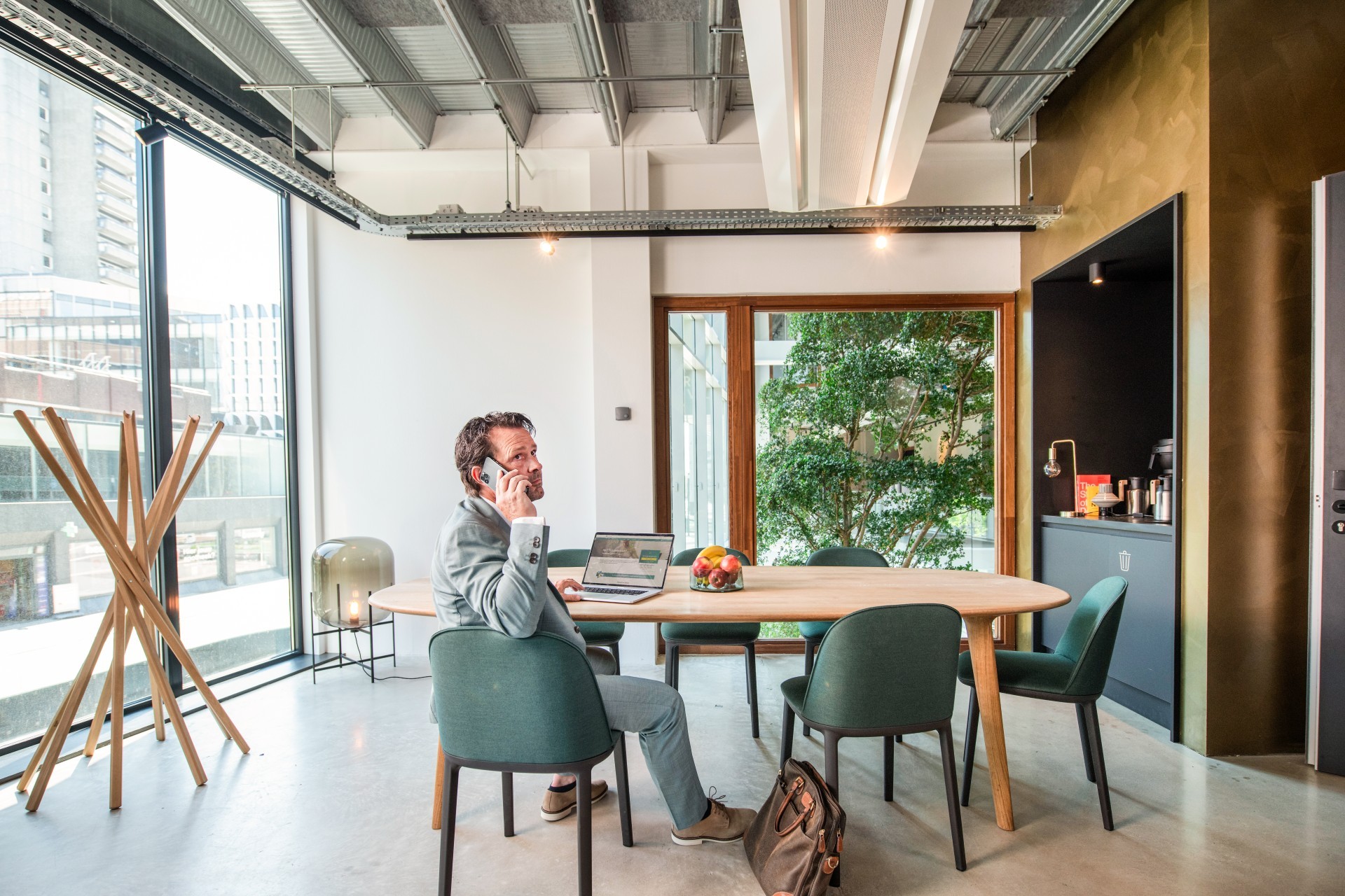 Man in pak zit achter zijn laptop met telefoon aan zijn oor