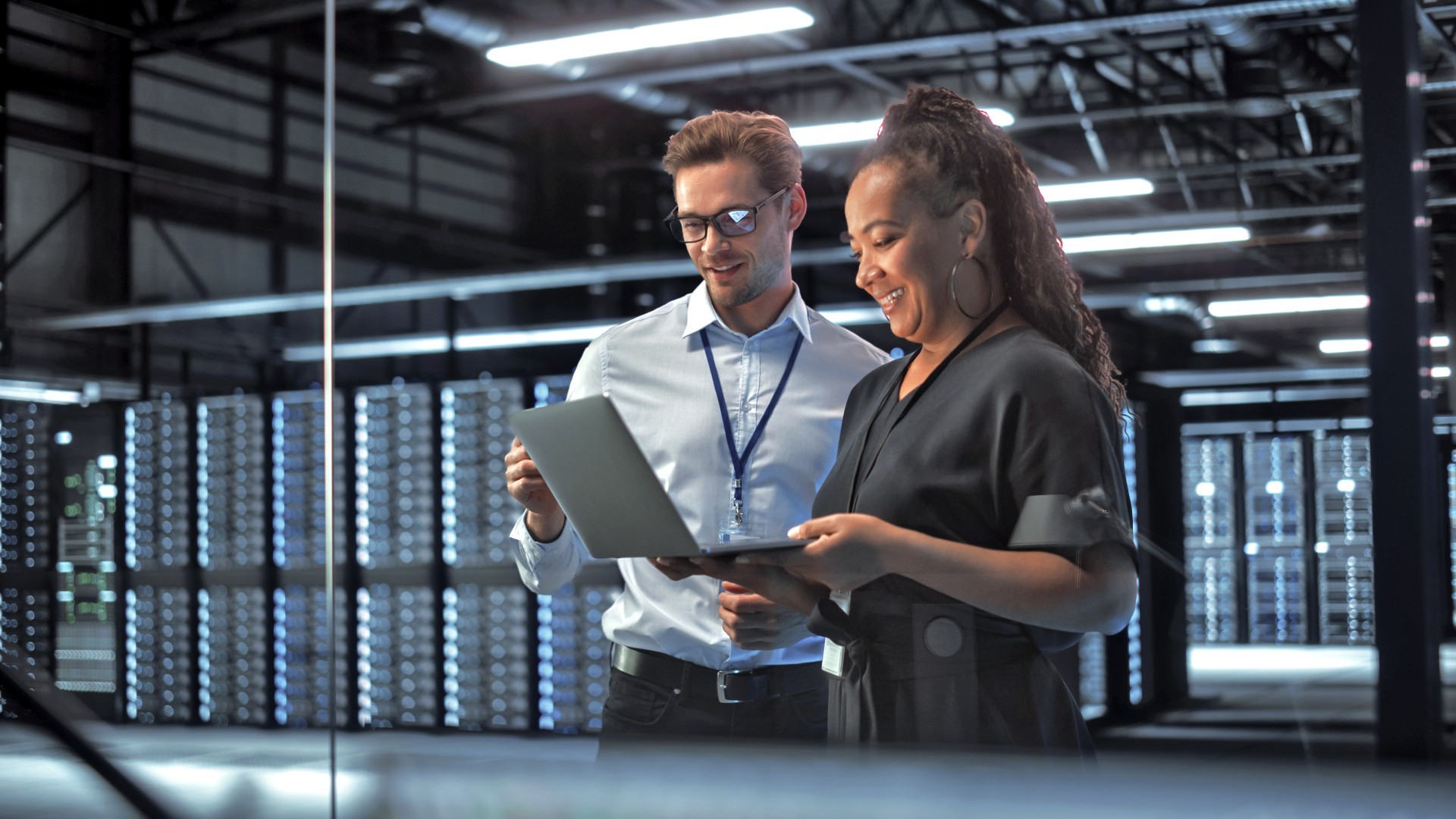 In een datacenter kijken twee mensen op hun laptop. Op de achtergrond staan grote serverracks.