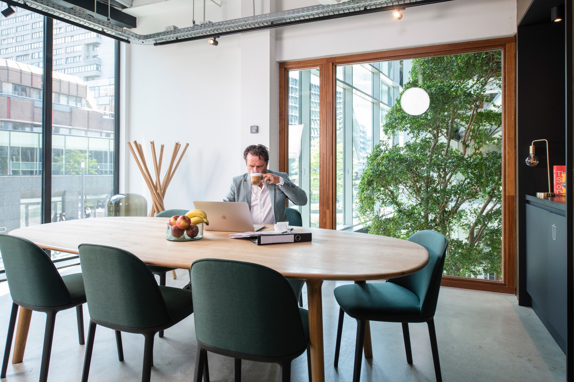Man in pak zit achter zijn laptop en drinkt een kop koffie
