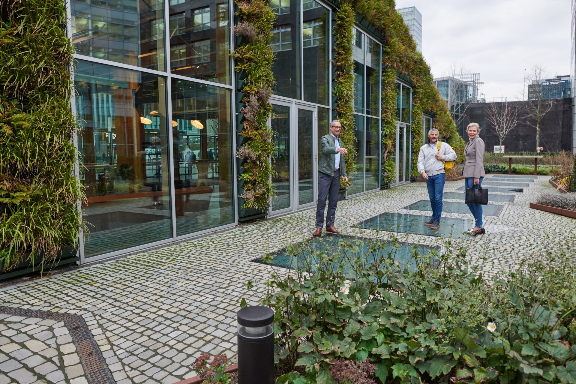 Drie mensen staan bij bedrijfspand met veel glas en groen