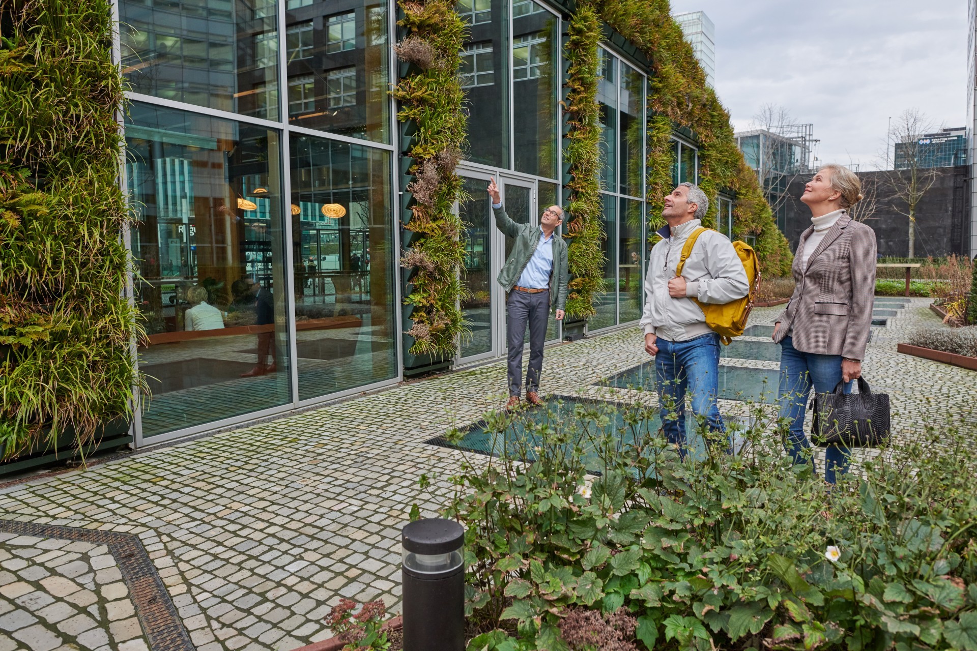 Drie mensen kijken naar een bedrijfspand. Aan de buitenkant van het pand groeien planten.