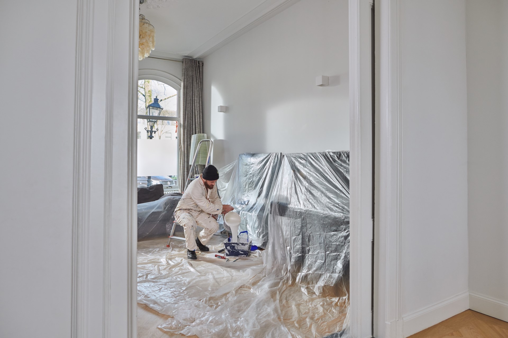 Schilder giet verf over in verfbak. Vloer is beschermd met folie.