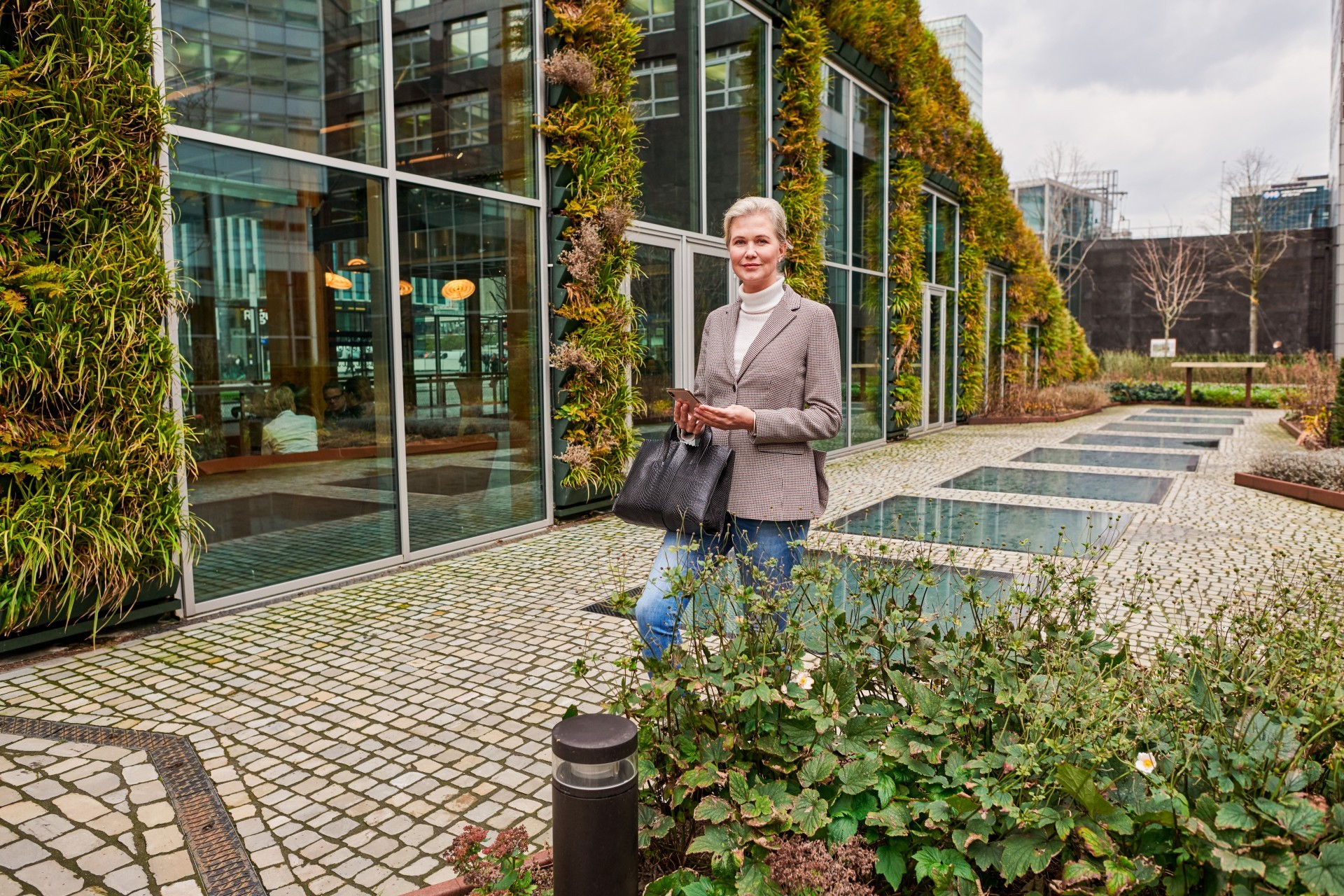 Vrouw in zakelijke kleding staat voor bedrijfspand waar planten langs groeien