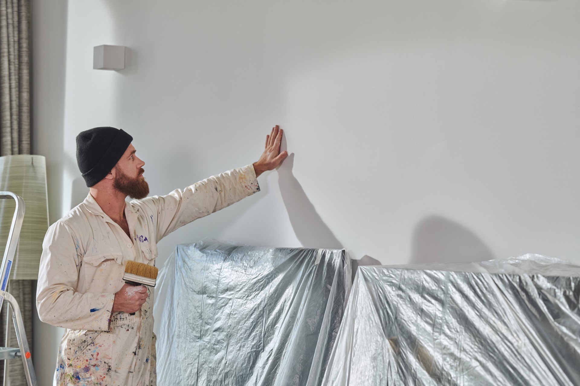 Schilder staat voor muur met in folie beschermde meubels