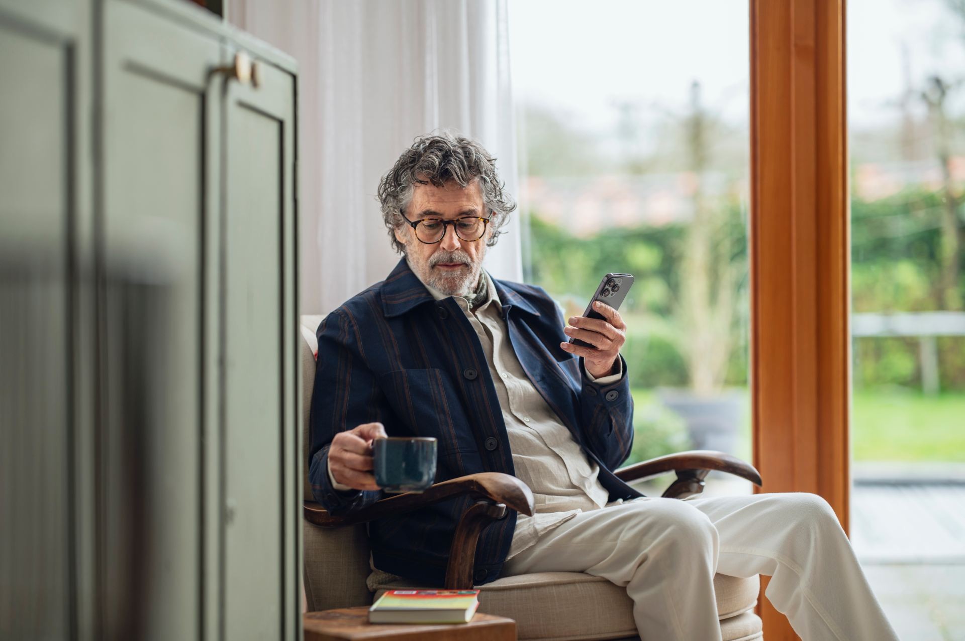 Man pakt zijn kop koffie terwijl hij iets uitzoekt op zijn mobiele telefoon